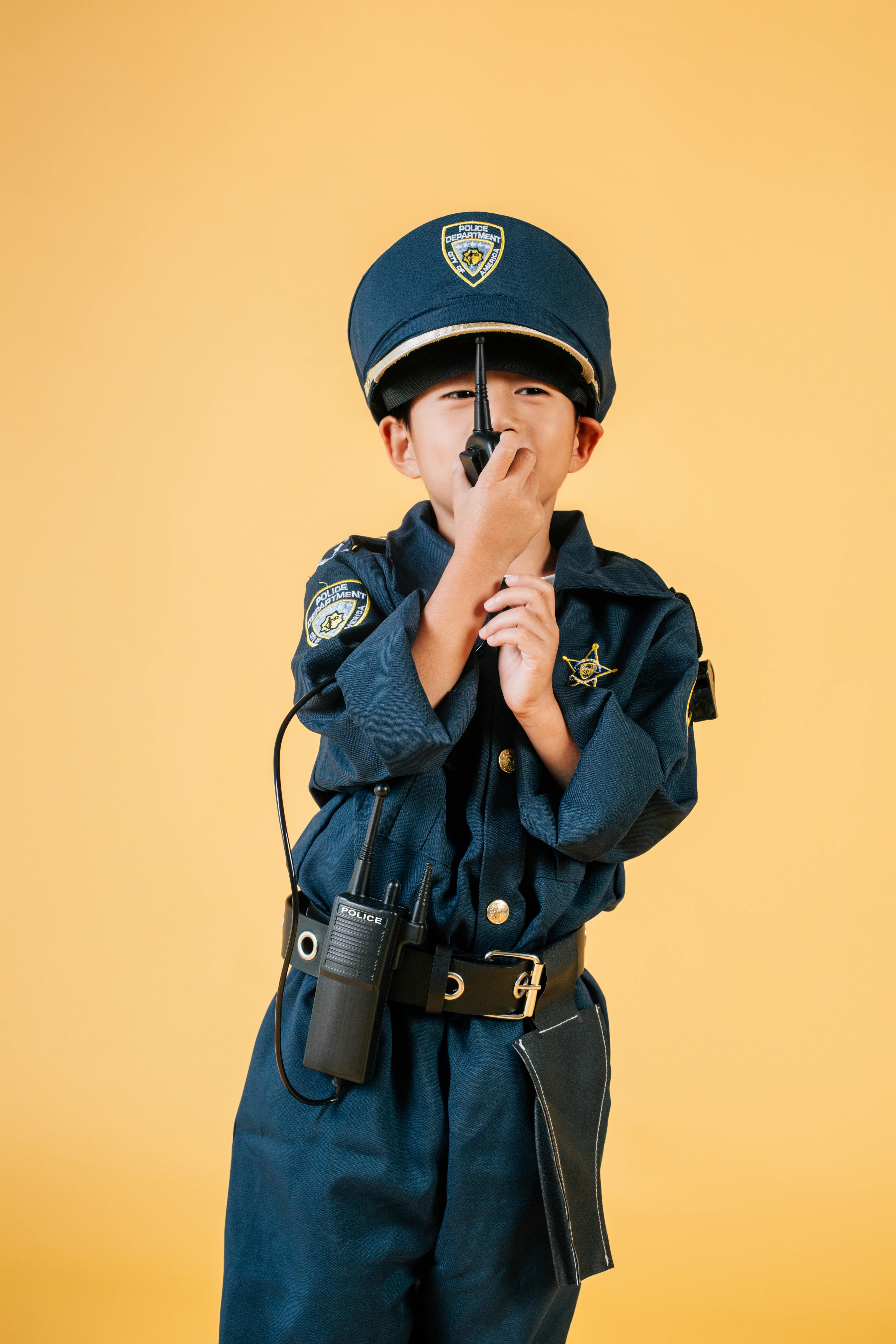 Child dressed as a police officer communicating via radio on a vibrant yellow background.
